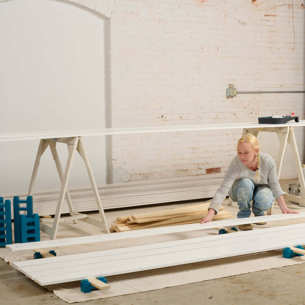 PaintBlox Pro drying blocks supporting long painted boards on a workbench for efficient drying.