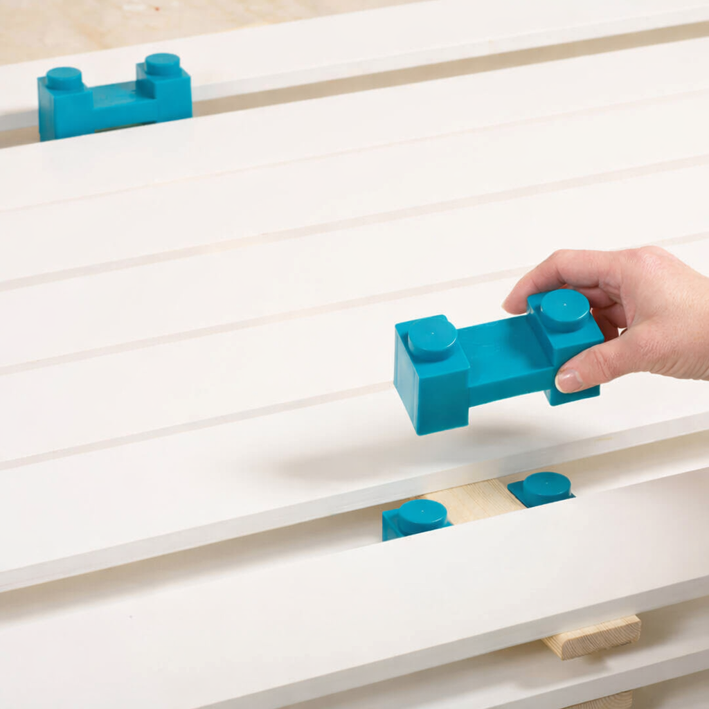 Hand placing a blue PaintBlox on the  modular drying rack system to support the next layer of boards painted white