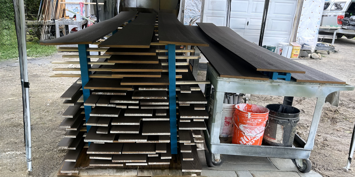 Composite trim drying outdoors under a canopy on PaintBlox Pro supports